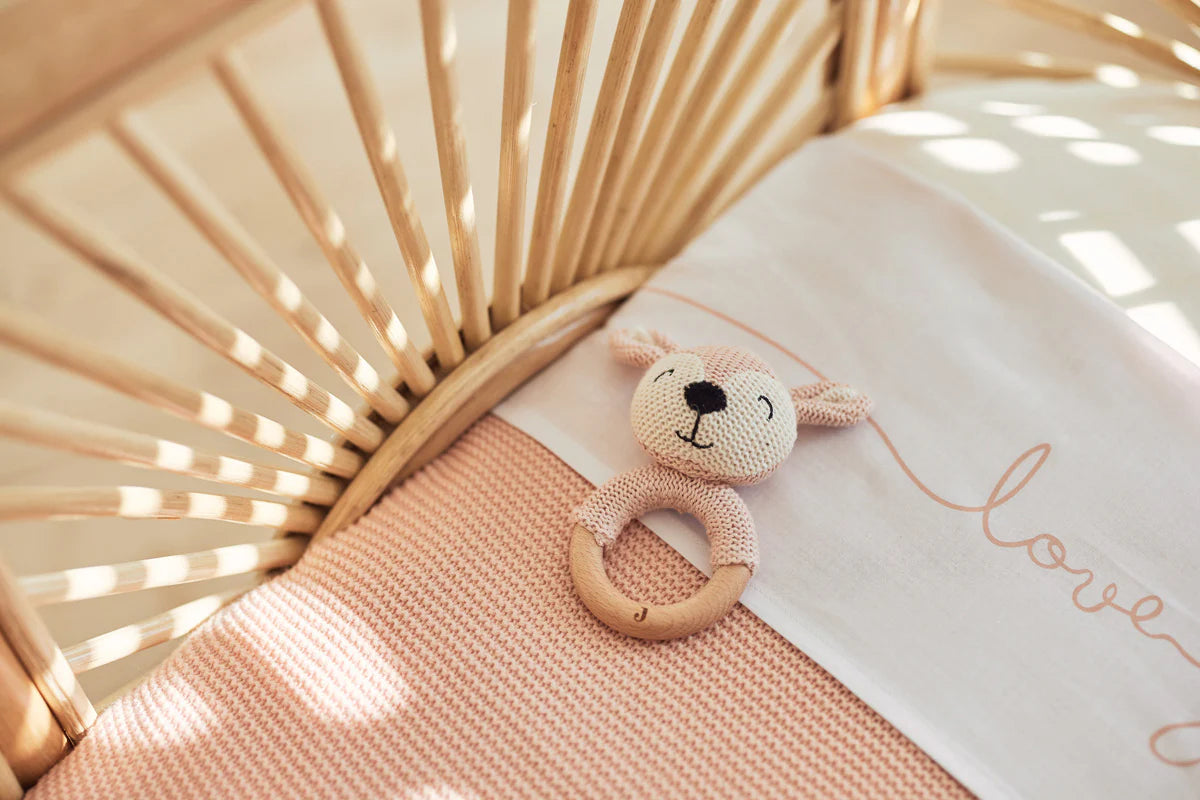 Jollein Bijtring Deer Pale Pink in wieg op roze gebreide deken, ideaal als baby speelgoed en cadeau.
