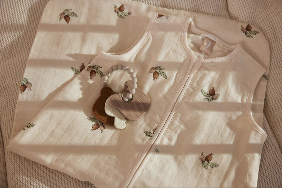 Jollein Bijtring Teddy Bear ligt op crème slaapzak met print, perfect als natuurlijk kraamcadeau of baby cadeau.