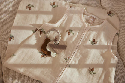 Jollein Bijtring Teddy Bear ligt op crème slaapzak met print, perfect als natuurlijk kraamcadeau of baby cadeau.