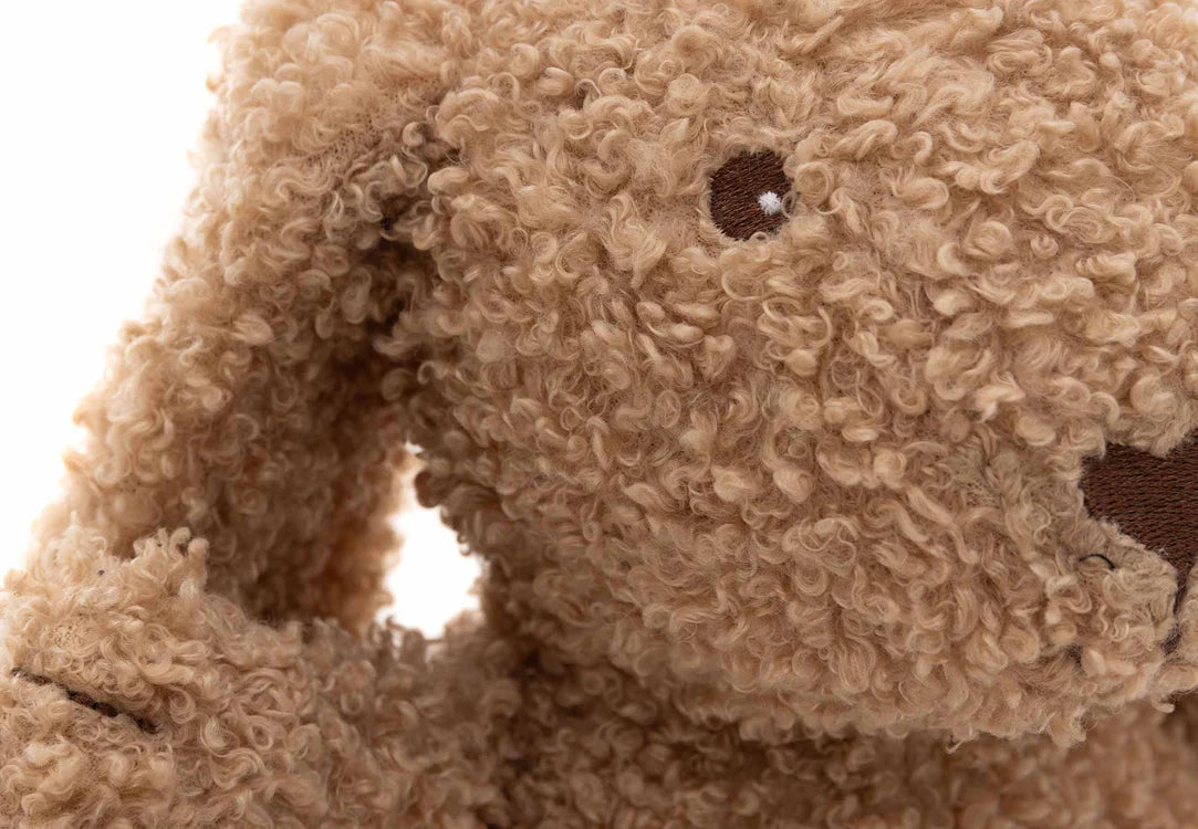 Close-up van gezicht Jollein Knuffel Bunny in biscuitkleur met geborduurde oogjes en zachte teddy vacht.