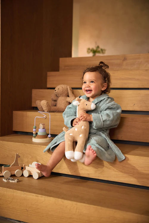 Kind knuffelt met Jollein giraffe van zachte stof in biscuitkleur op de trap, leuk kraamcadeau.