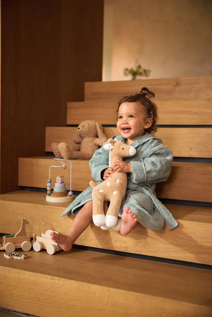 Kind knuffelt met Jollein giraffe van zachte stof in biscuitkleur op de trap, leuk kraamcadeau.