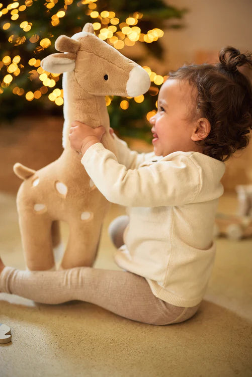 Peuter speelt met Jollein XL giraffe knuffel in biscuitkleur bij kerstboom, geschikt als speelgoed en cadeau.