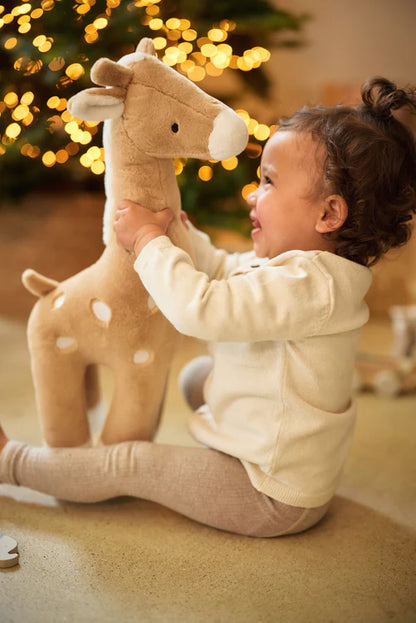 Peuter speelt met Jollein XL giraffe knuffel in biscuitkleur bij kerstboom, geschikt als speelgoed en cadeau.