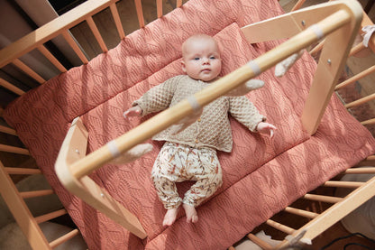 Baby ligt in houten wieg onder Jollein babygym met maan speeltjes in beige kleur, ideaal baby speelgoed.