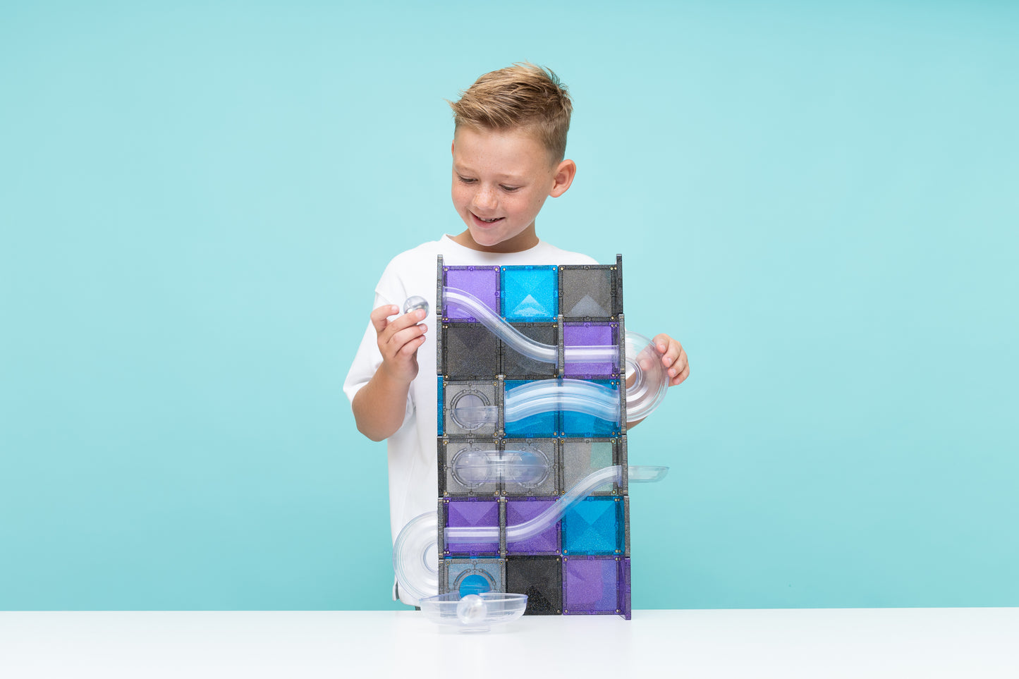 Jongen bouwt hoge toren met Connetix magneet speelgoed knikkerbaan in ruimte kleuren en transparant