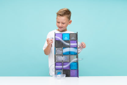 Jongen bouwt hoge toren met Connetix magneet speelgoed knikkerbaan in ruimte kleuren en transparant