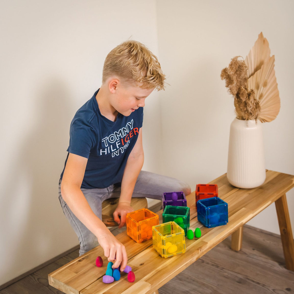 Jongen sorteert gekleurde magneten Coblo speelgoed op houten bankje, leren door creatief spelen