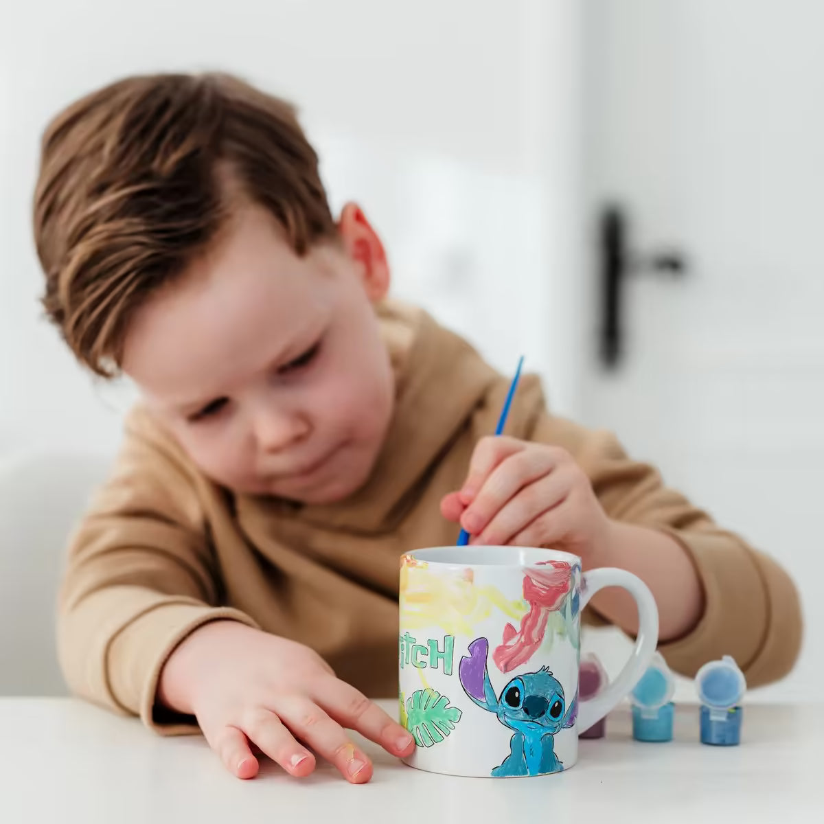 Jongen schildert Disney Stitch mok met Totum verfset, vrolijk knutsel idee en activiteit om te knutselen met peuters.