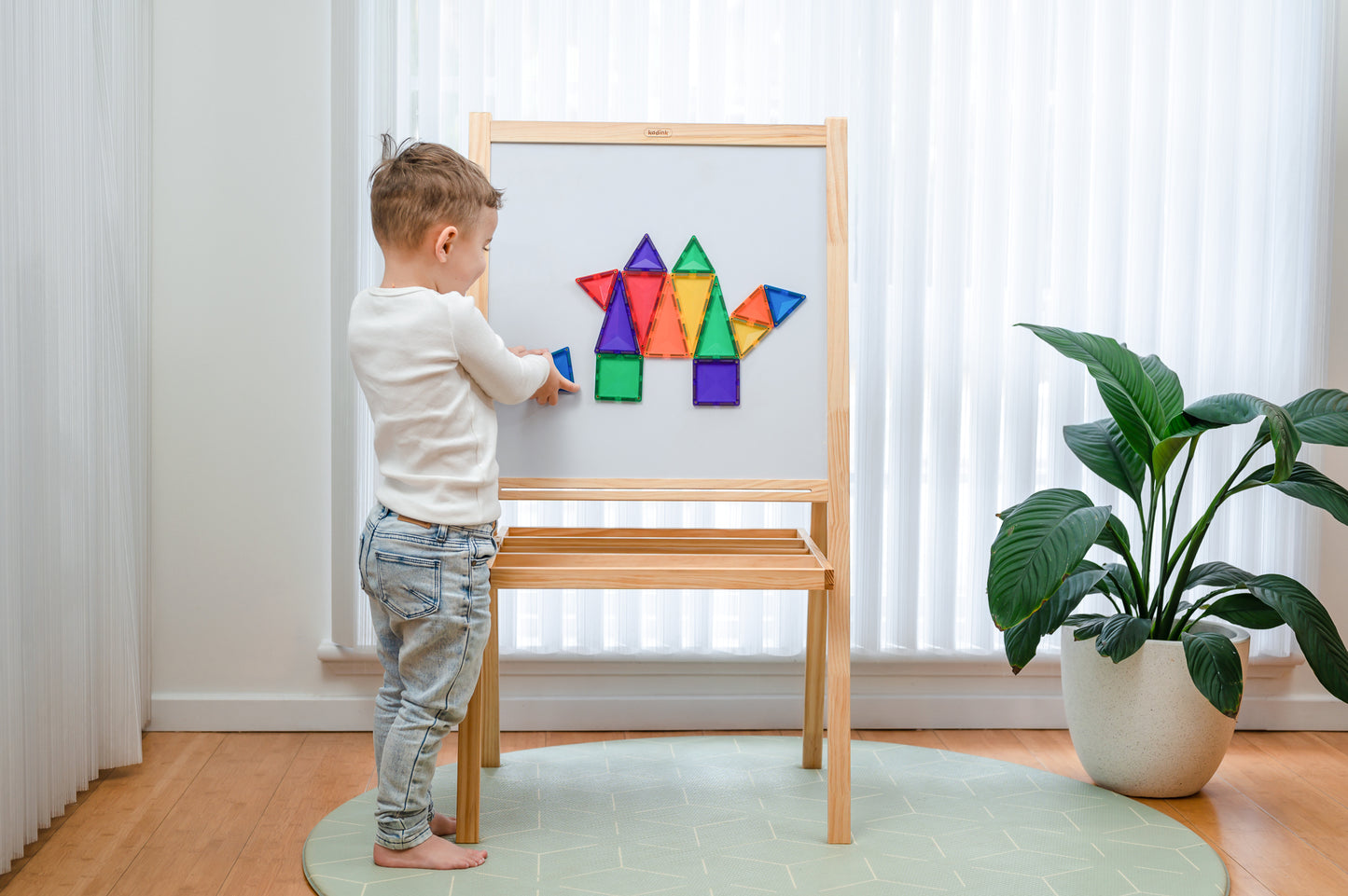 Kind bouwt dinosaurus Connetix tiles op magneetbord houten frame lichte kinderkamer vloer