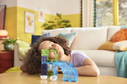 Kind kijkt geconcentreerd naar haar bouwwerk van magnetisch speelgoed met hamster en blauwe glijbaan.