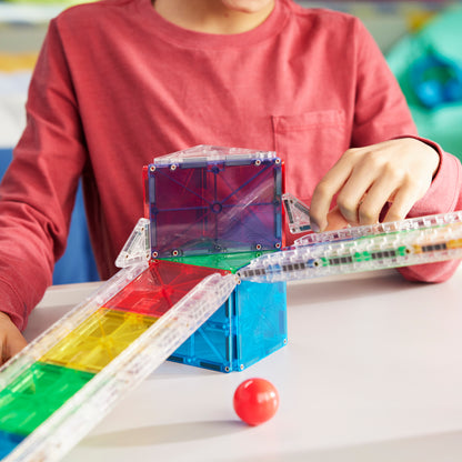 Kind bouwt magnetic magna tiles Rail Racers knikkerbaan met kleurrijke magnetische tegels en knikker
