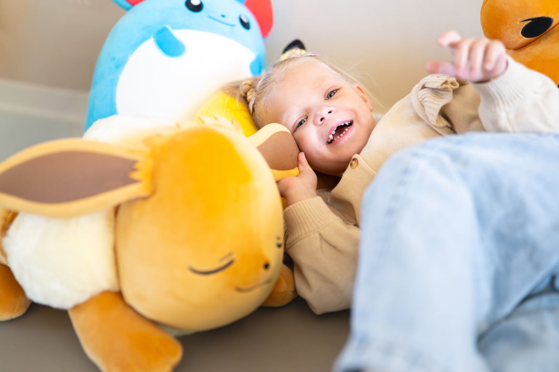 Kind speelt vrolijk met grote Eevee knuffel omringd door andere Pokemon knuffels als baby speelgoed