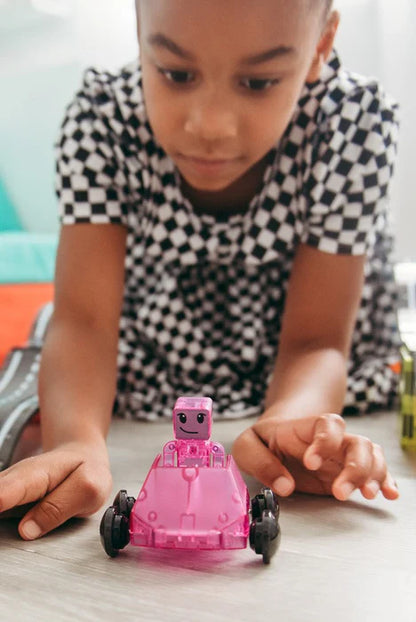 Kind in geruite jurk speelt met een roze robot en een magnetische set van Magna Tiles Dashers op de vloer.