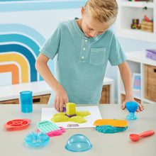 Jongen speelt met Super Sandisfying Set van Kinetic Sand, bouwt gele vormen aan tafel; educatief speelgoed in actie.