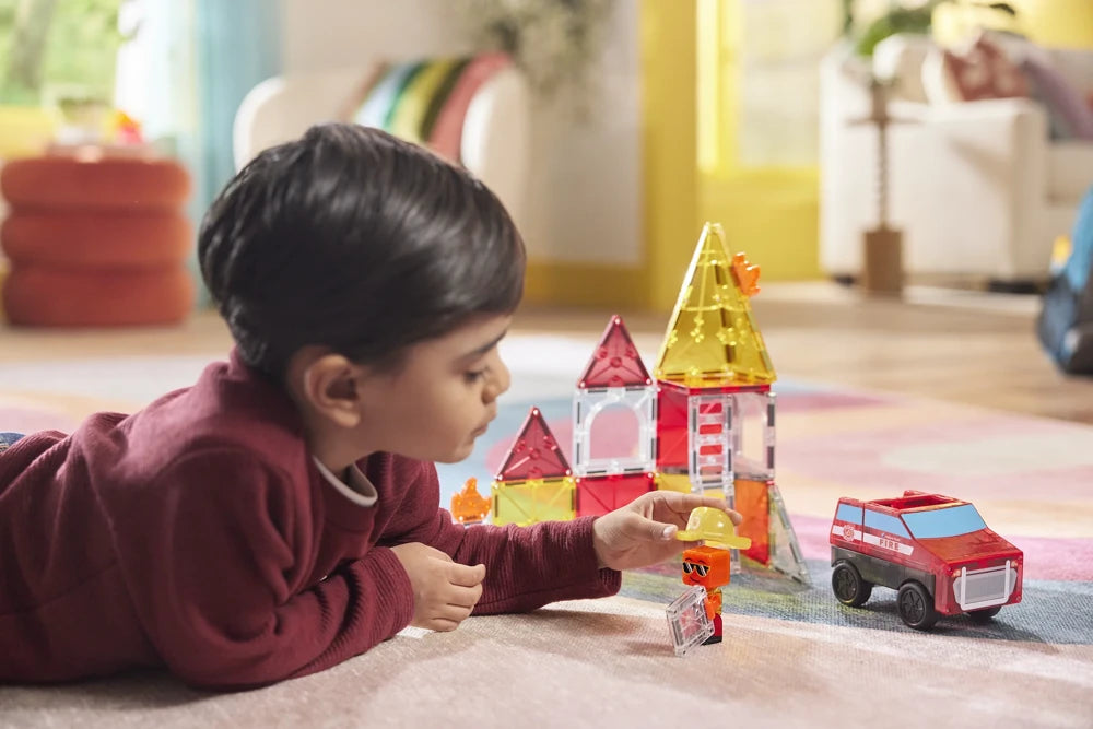 Jongen ligt op de grond en speelt met de magnetische brandweerset van Magna Tiles en bijhorende accessoires.
