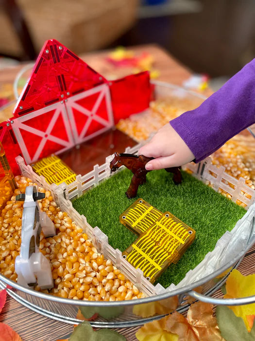 Kind speelt met magnetic magna tiles boerderij en farm animals in sensorische speelbak met maïs