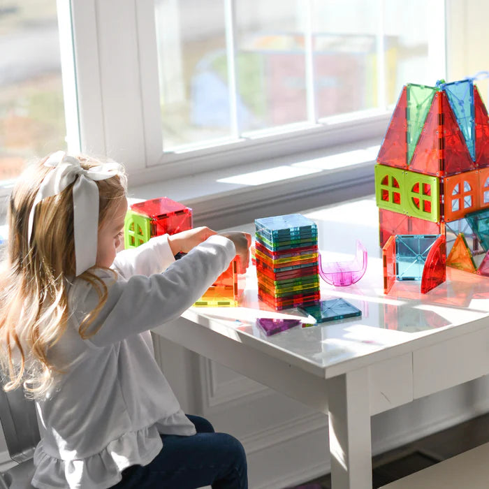 Kind speelt met de Magnetic Magna Tiles Metropolis Set - 110 magnetic bouwstenen op een witte tafel bij een helder raam.