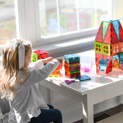 Kind speelt met de Magnetic Magna Tiles Metropolis Set - 110 magnetic bouwstenen op een witte tafel bij een helder raam.