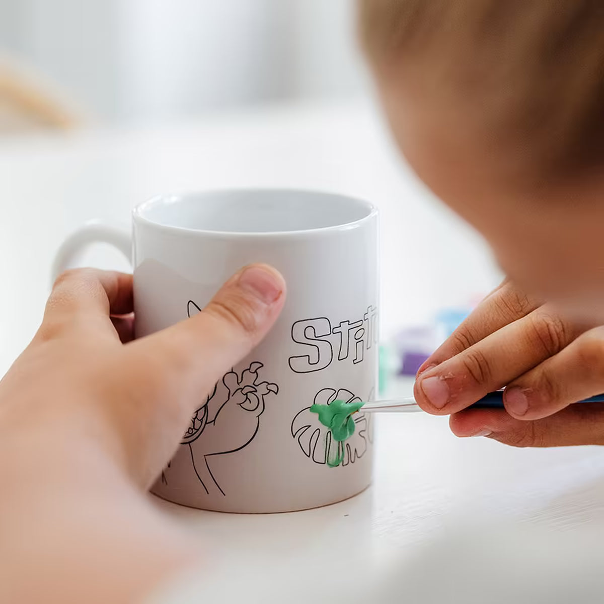 Kind verft groen blad op Disney Stitch mok uit Totum set, leuk knutsel idee en geschikt om met peuters knutselen thuis.