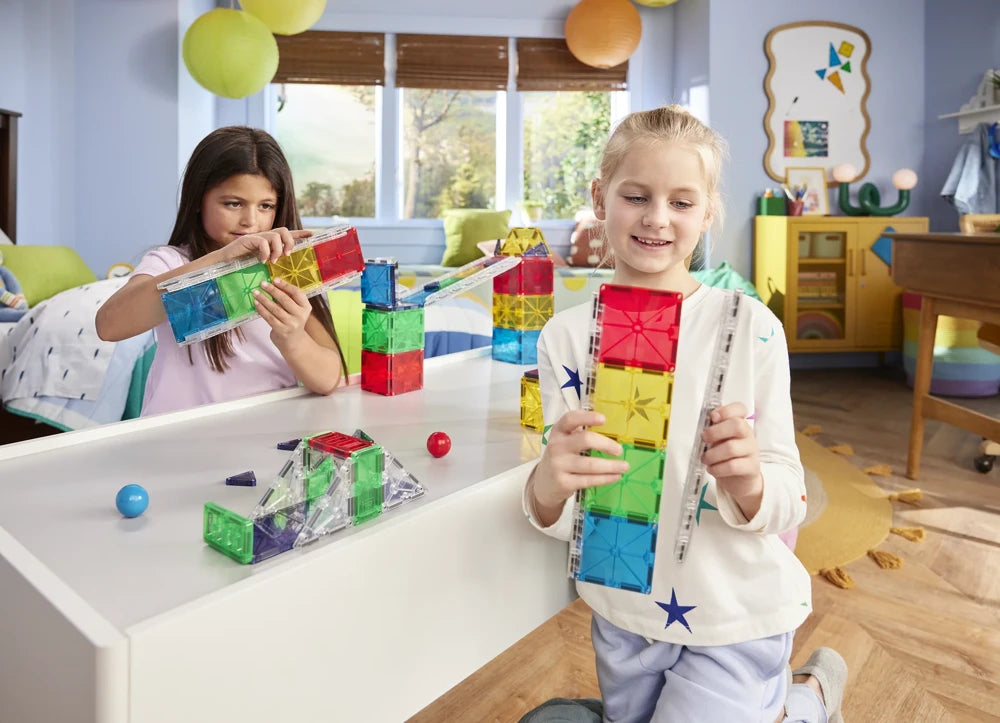 Twee kinderen bouwen met 90 magnetische tegels een kleurrijke magna tiles knikkerbaan in de kinderkamer.