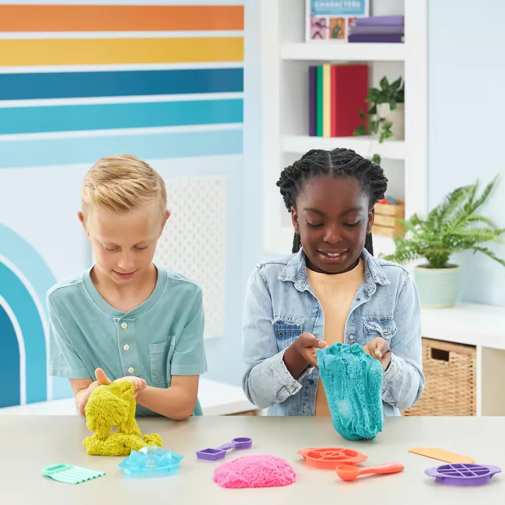 Jongen en meisje kneden geel en blauw Kinetic Sand aan tafel, ontdekken sensorisch speelgoed en fijne motoriek.