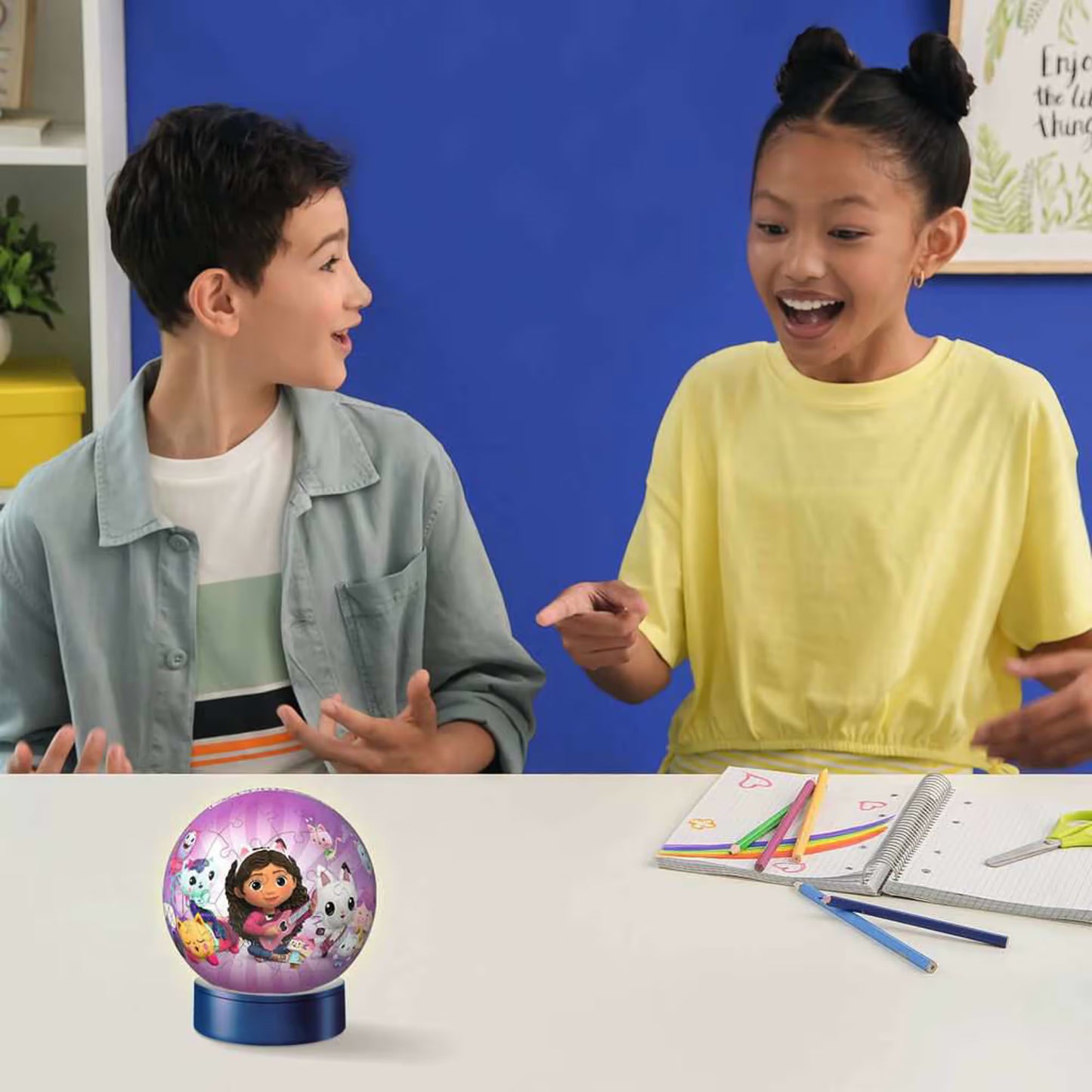 Twee kinderen spelen enthousiast met Ravensburger 3D puzzel Gabby’s Dollhouse nachtlampje kind aan tafel.