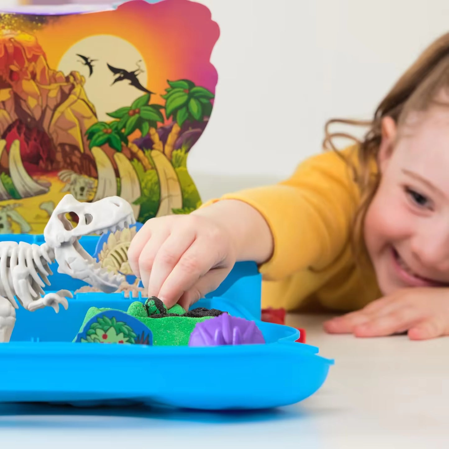 Een lachend kind dat speelt met Kinetic Sand en een dino-skelet in de Trex Dino Case speelset, plezier met sensorisch speelgoed.
