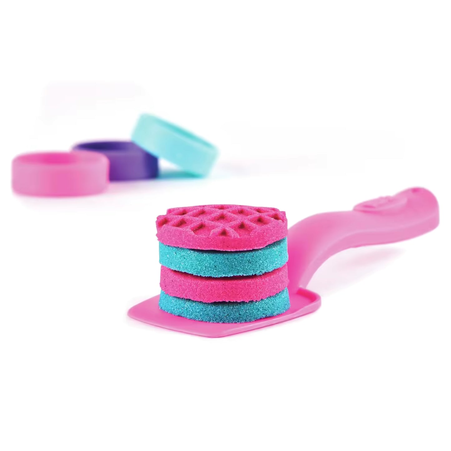 Stapel kleurrijke zandtaartjes van Kinetic Sand op roze spatel, creatief speelgoed voor fantasierijk spelen.