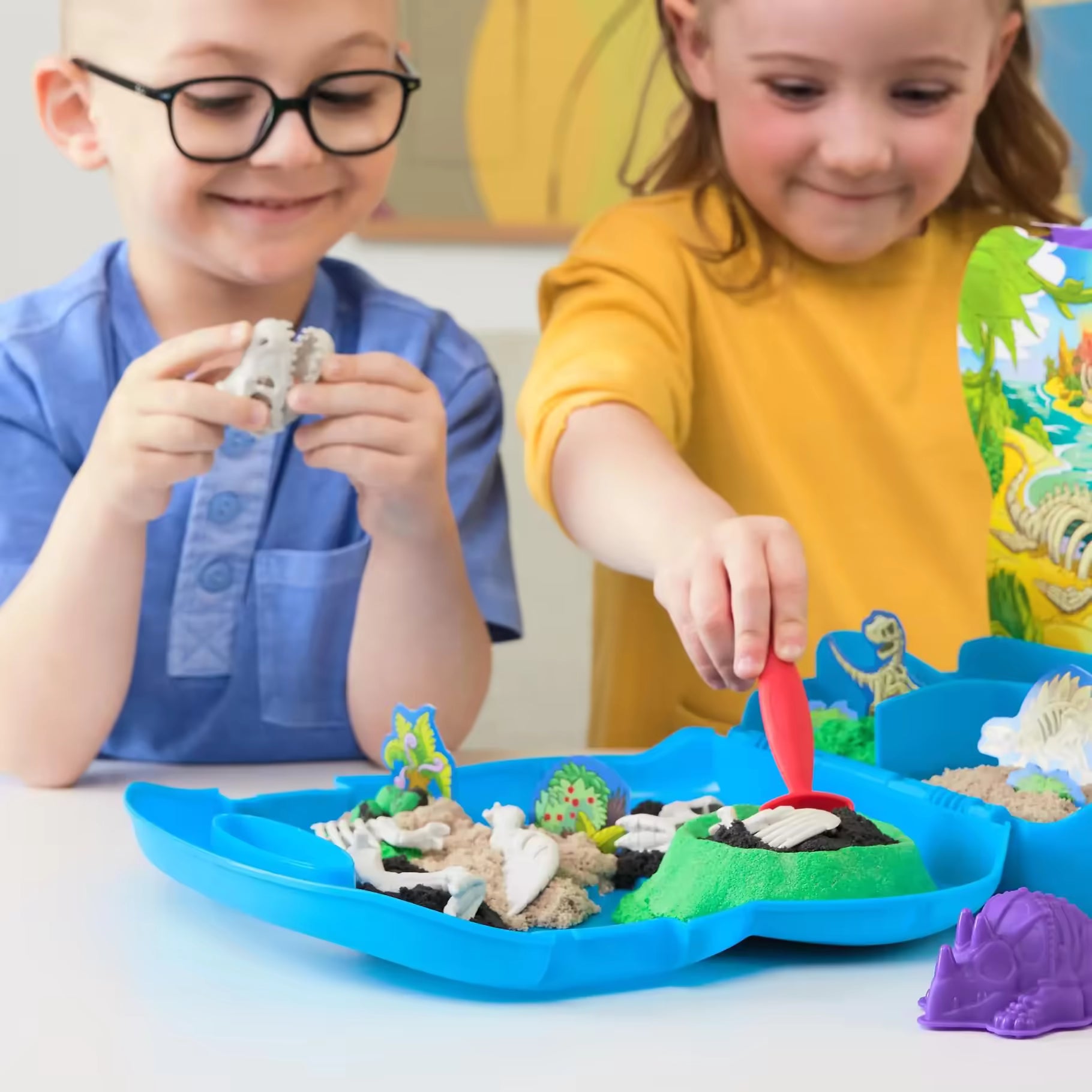 Twee kinderen spelen met Kinetic Sand, waarbij ze de Trex Dino Case gebruiken om zand en dino-skeletten te verkennen, geweldig educatief speelgoed.
