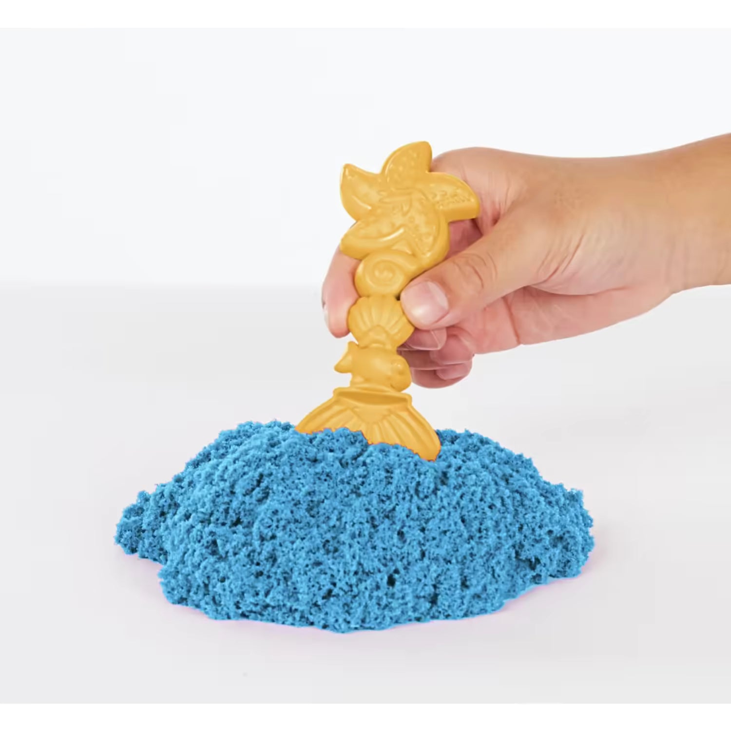 Close-up van gouden schelpvormige tool in blauw Kinetic Sand, leuk en educatief sensorisch speelgoed voor peuters en kleuters.