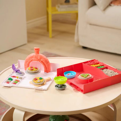 Squishpizza set van kinetisch zand met oven, bakaccessoires en pizza’s op een ronde houten tafel.