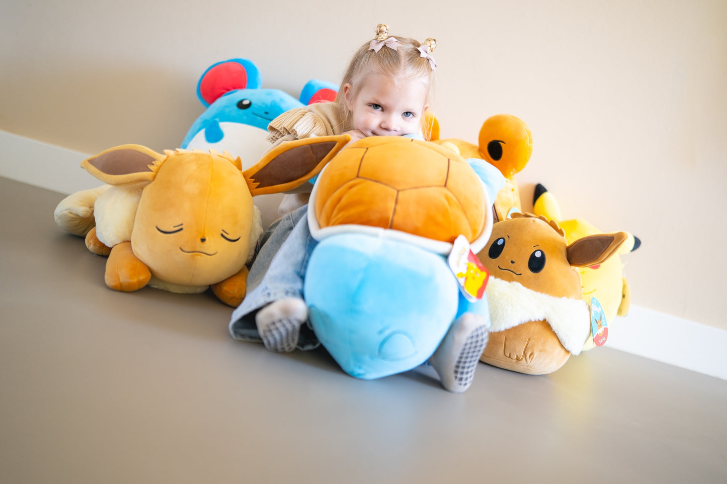 Knuffel collectie met Pokemon zoals Eevee en Squirtle tussen meisje op bed, ideaal kraamcadeau