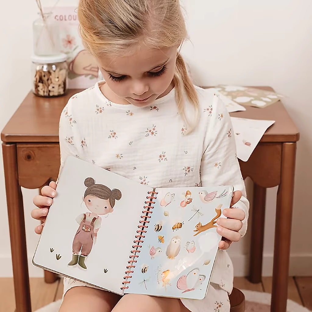 Klein meisje leest het Little Dutch aankleedboek Fairy Garden, met stickers en figuren, ideaal kinderboek voor creatieve peuters.