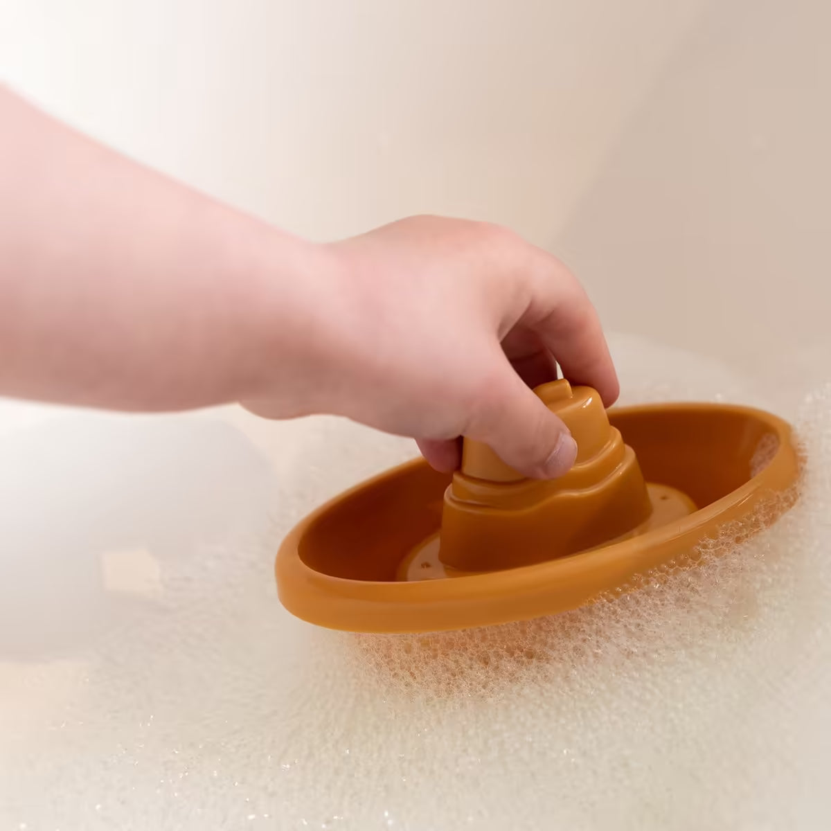 Kind speelt met geel Little Dutch Bad Bootje in schuimbad, vrolijk badspeelgoed voor peuters en kleuters.