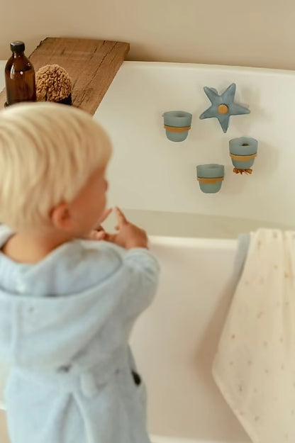 Kind kijkt naar Little Dutch Badwand bekers zeester, drie blauwe bekers en ster waterwiel bevestigd aan badwand.