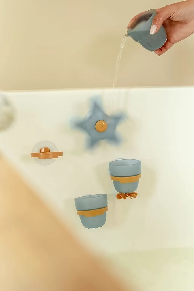 Hand giet water in Little Dutch Badwand bekers zeester, blauwe bekers en ster draaien vrolijk, badspeelgoed voor peuters.