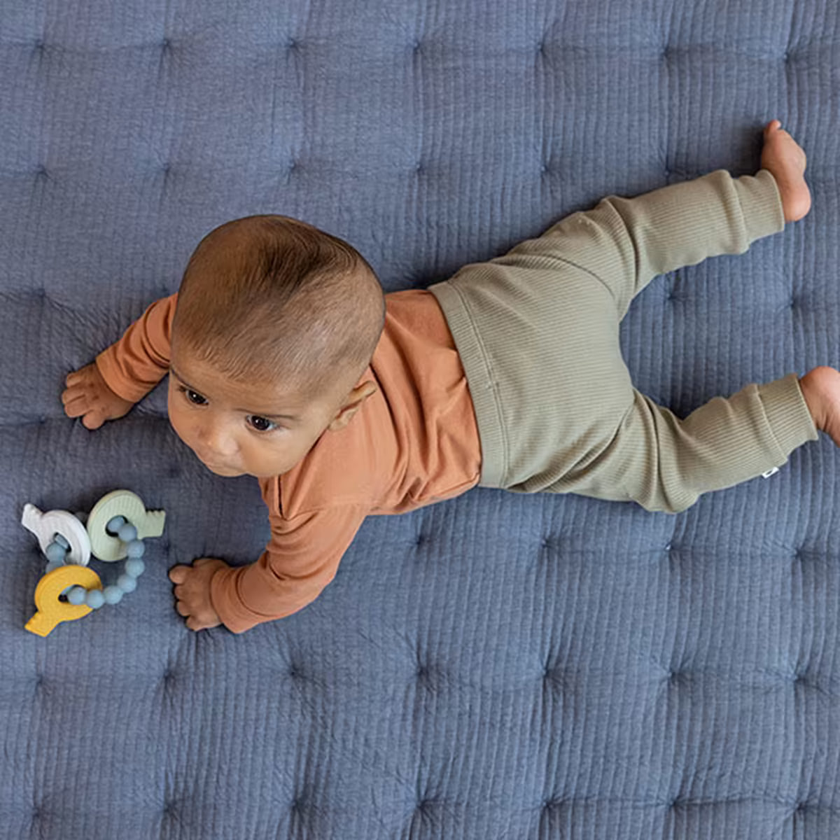 Baby ligt op buik naast Little Dutch Bijtring siliconen sleutelbos in blauw en pastel, leuk baby speelgoed en kraamcadeau.