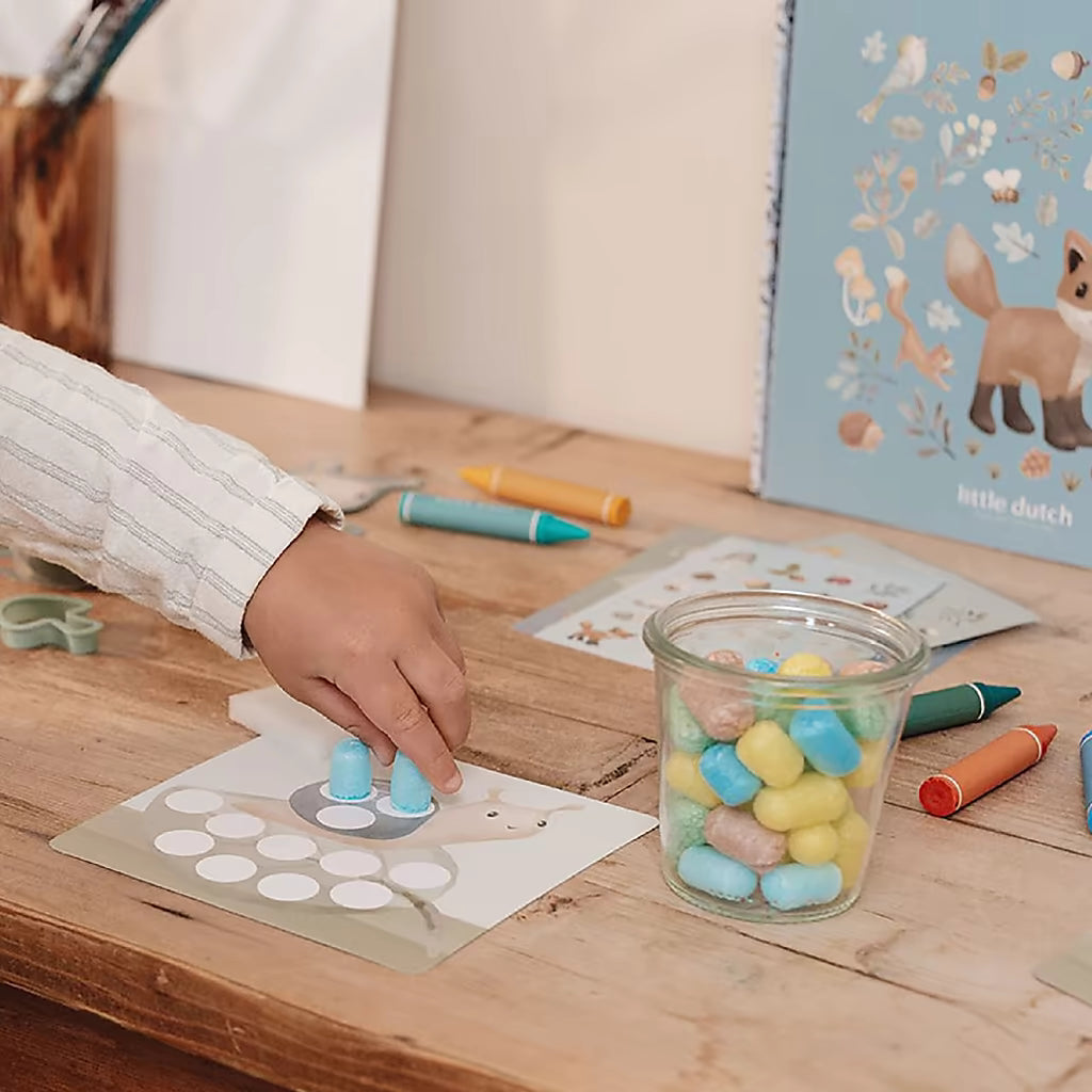 Hand van een kind plaatst gekleurde stukjes op slak figuur uit de Little Dutch Knutseldoos Forest Friends.