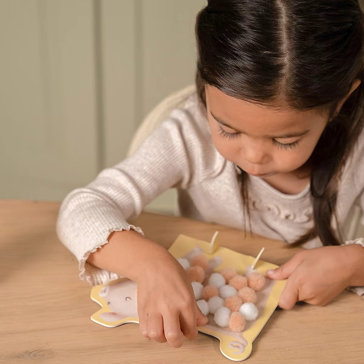 Detailfoto kind dat Little Dutch pompom plakt op varken, een creatief knutsel idee voor peuters.