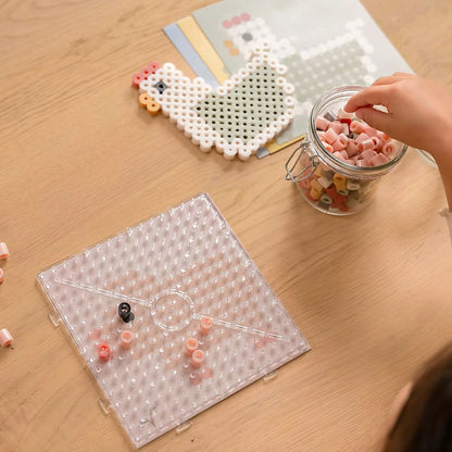 Kind kiest kralen naast voorbeeldkaart en afgewerkte kip met Little Dutch Strijkkralen Maxi Little Farm.