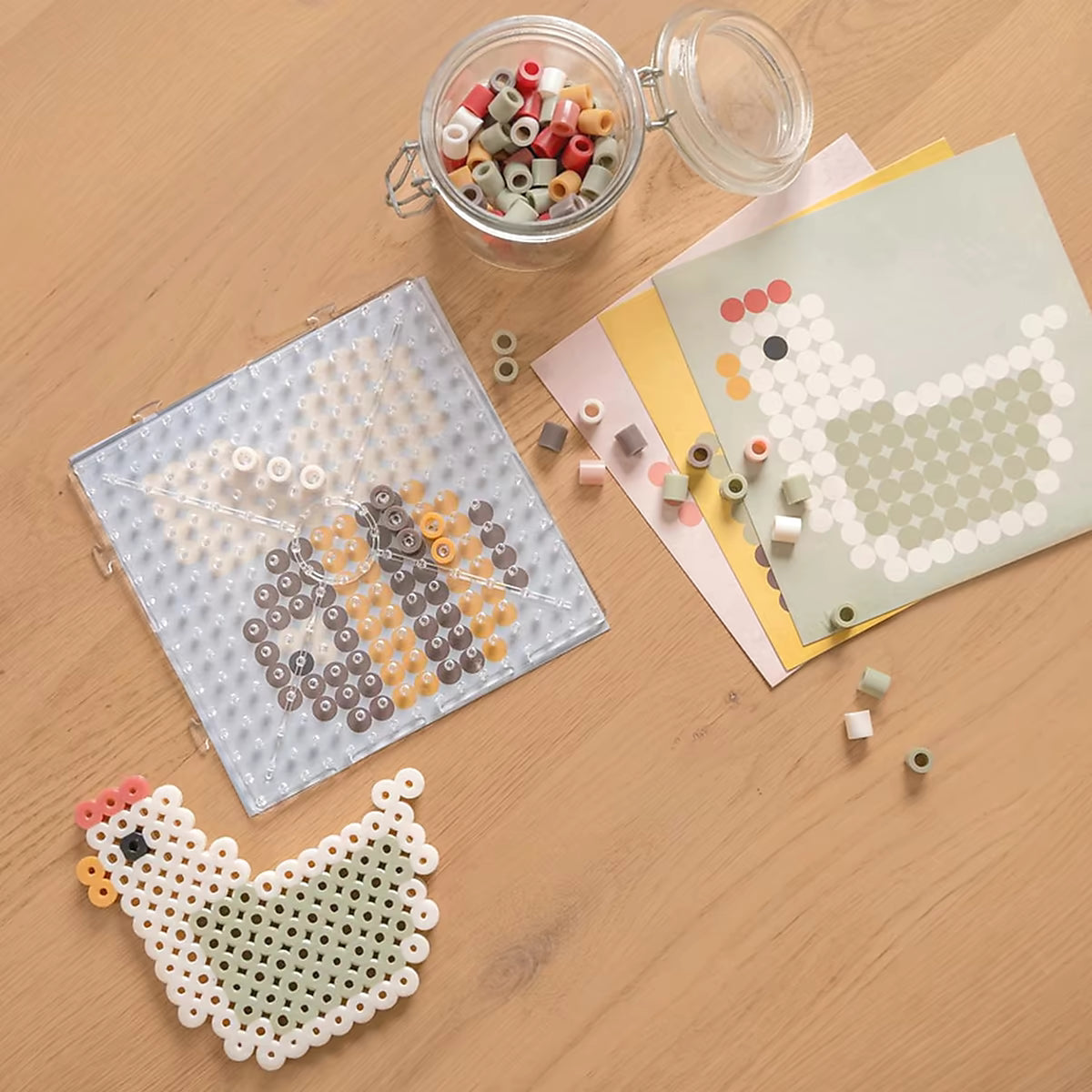 Bovenaanzicht strijkplaat met bij en voorbeeldkaarten naast kip, gemaakt met Little Dutch Strijkkralen Maxi Little Farm.