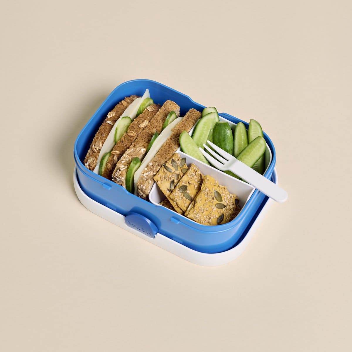Blauwe lunchbox met bento-indeling, gevuld met brood en groente, inclusief vorkje en perfect voor kinderen