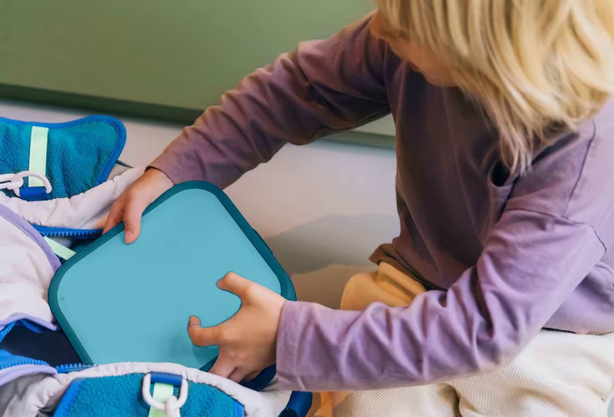 Kind plaatst blauwgroene Mepal lunchbox in rugzak, handige en kindvriendelijke lunchoplossing voor school of uitje.