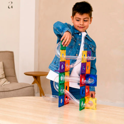 Jongen construeert coblo magnetische knikkerbaan met kleurige tegels en doorzichtige knikkerglijbaan