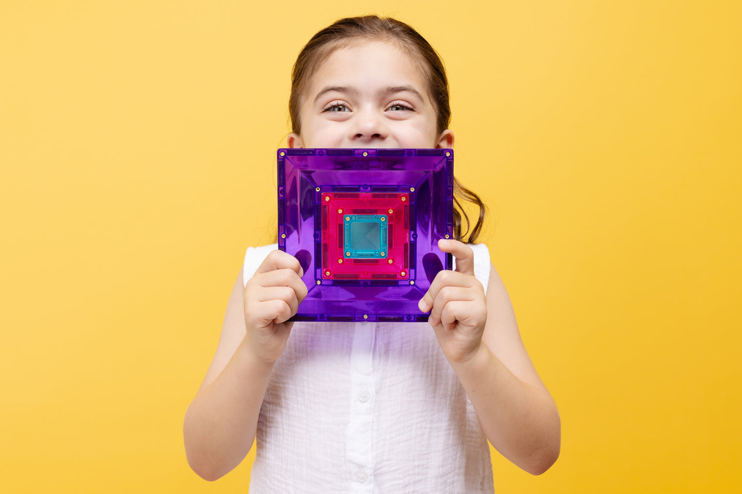 Meisje houdt kleurrijke magnetische tegel van Connetix Bright Portal Pack 48pc voor haar gezicht