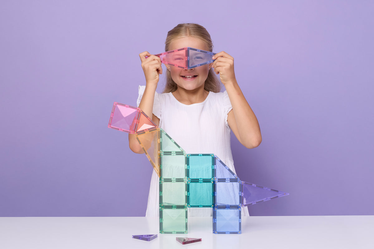 Kind met Connetix speelgoed pastel magneten speelgoed bouwt creatieve constructie paarse achtergrond