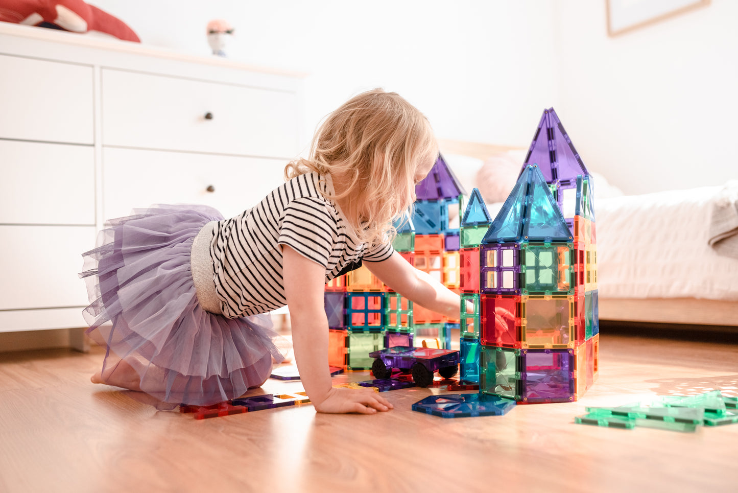 Magneten speelgoed meisje in tutu bouwt kasteel met connetix rainbow tiles op lichte kinderkamervloer