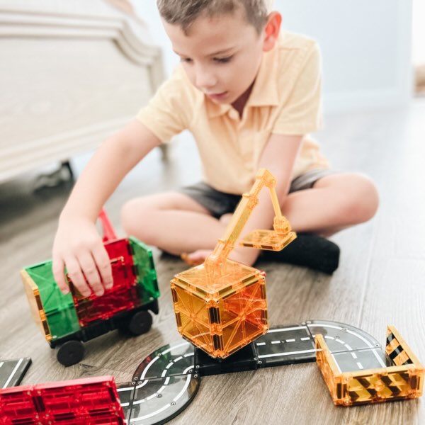 Jongen speelt op vloer met Magnetic Magna Tiles Builder set met kraan, wegdelen en vrachtwagen, magneet speelgoed binnen.