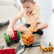 Jongen speelt op vloer met Magnetic Magna Tiles Builder set met kraan, wegdelen en vrachtwagen, magneet speelgoed binnen.